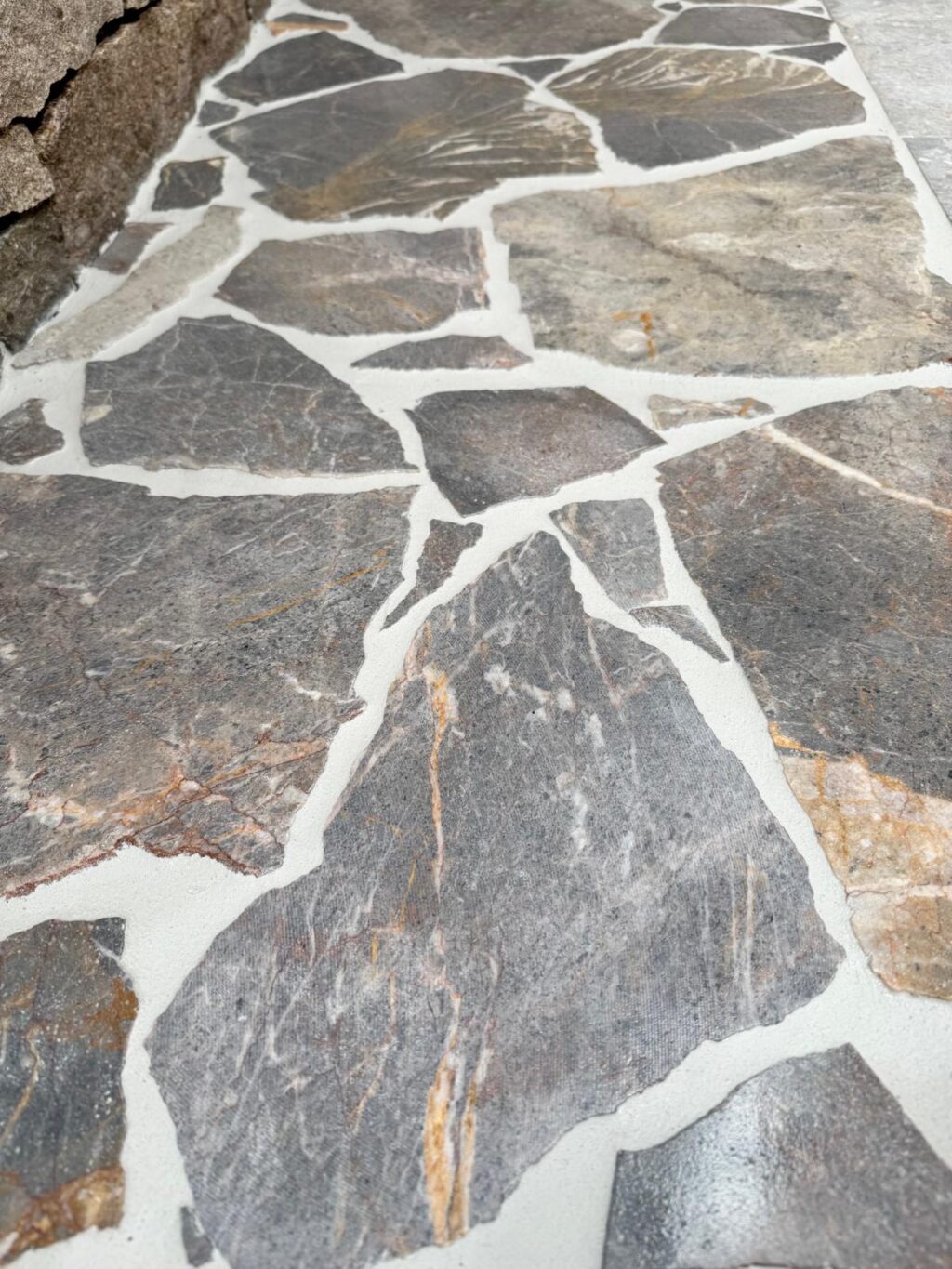 Irregular-cut Atmos Marble pieces laid in a natural crazy paving pattern with white grout and deep grey, brown, and rust tones.