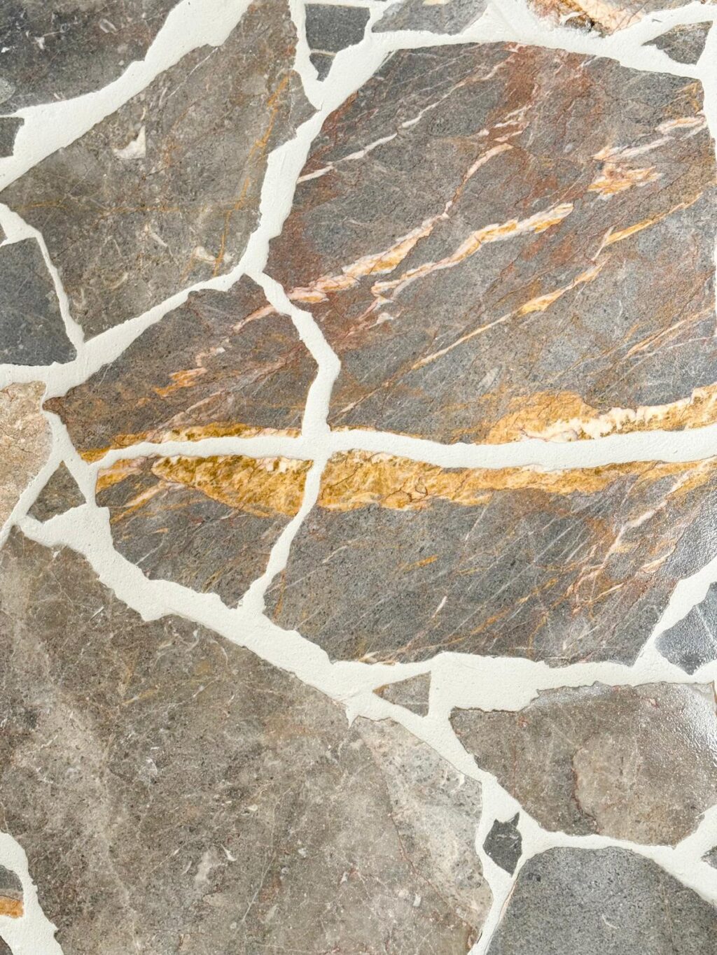 Atmos Marble laid in a crazy paving style with bold golden-orange and rust veining, separated by white grout.
