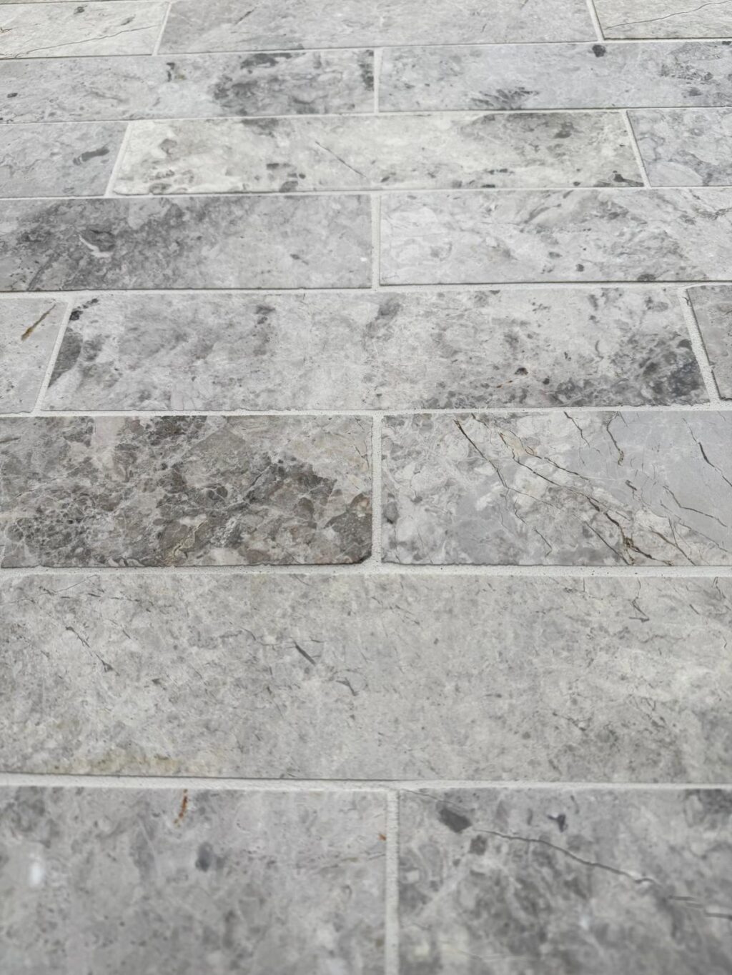 Close-up of Ocean Grey Marble tiles with a honed finish, showcasing varied grey tones and fine veining in a staggered layout.