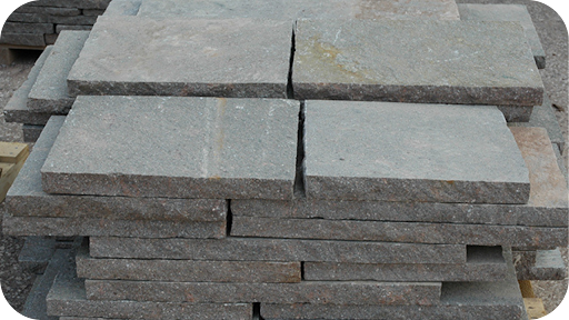 Stacked grey porphyry cobblestone slabs on site, showcasing strength, durability, and quality assurance from a trusted natural stone supplier.