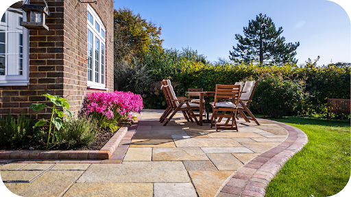 Outdoor patio with sandstone pavers, wooden dining set, and colourful flowers creating a warm, inviting garden space in Melbourne homes.