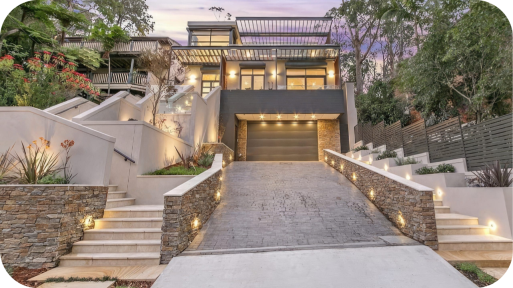 Contemporary home facade with stone cladding accents along stairs and driveway walls, highlighted by warm architectural lighting.