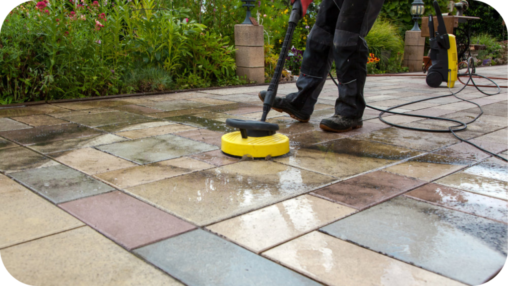 Worker pressure cleaning large outdoor pavers with a surface scrubber, refreshing a well-used stone courtyard area.