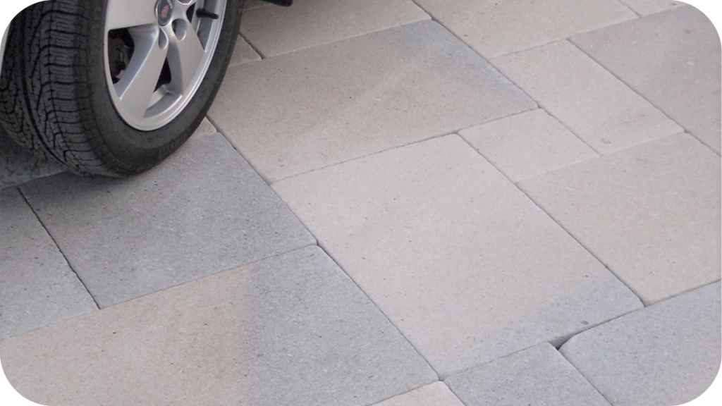 Light grey square pavers under the wheel of a parked car, showing strength and wear-resistance in heavy-use driveways.