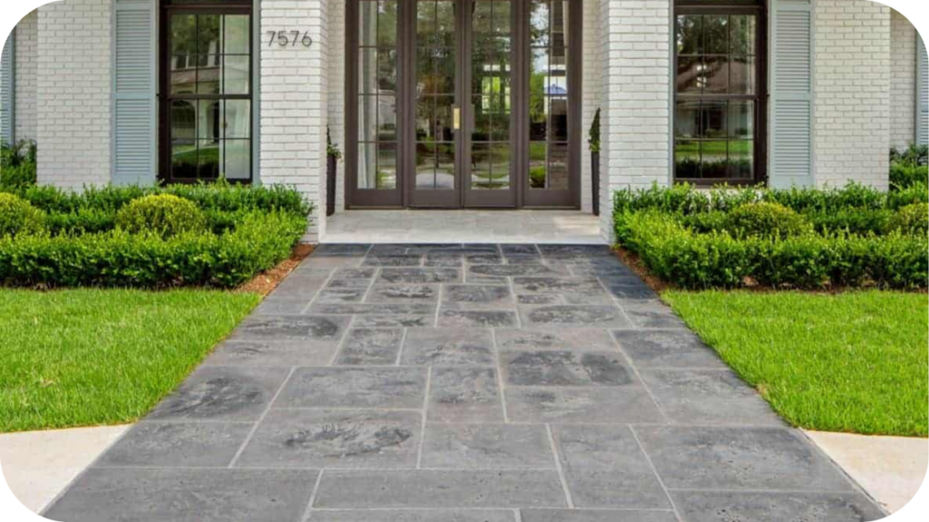 Front walkway paved with dark bluestone tiles, leading to a white brick home surrounded by manicured hedges and lawn.