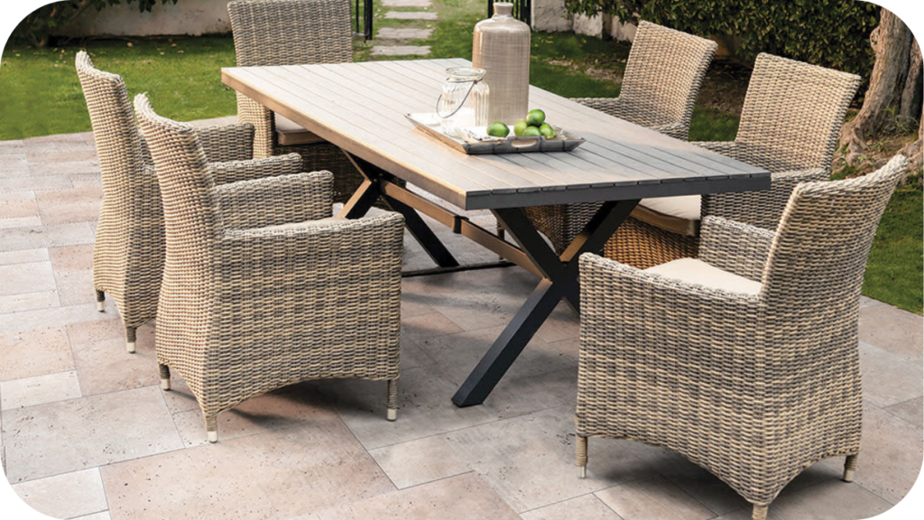Outdoor dining area with wicker chairs and wooden table set on stone pavers, styled with a jug, glasses, and fresh limes.