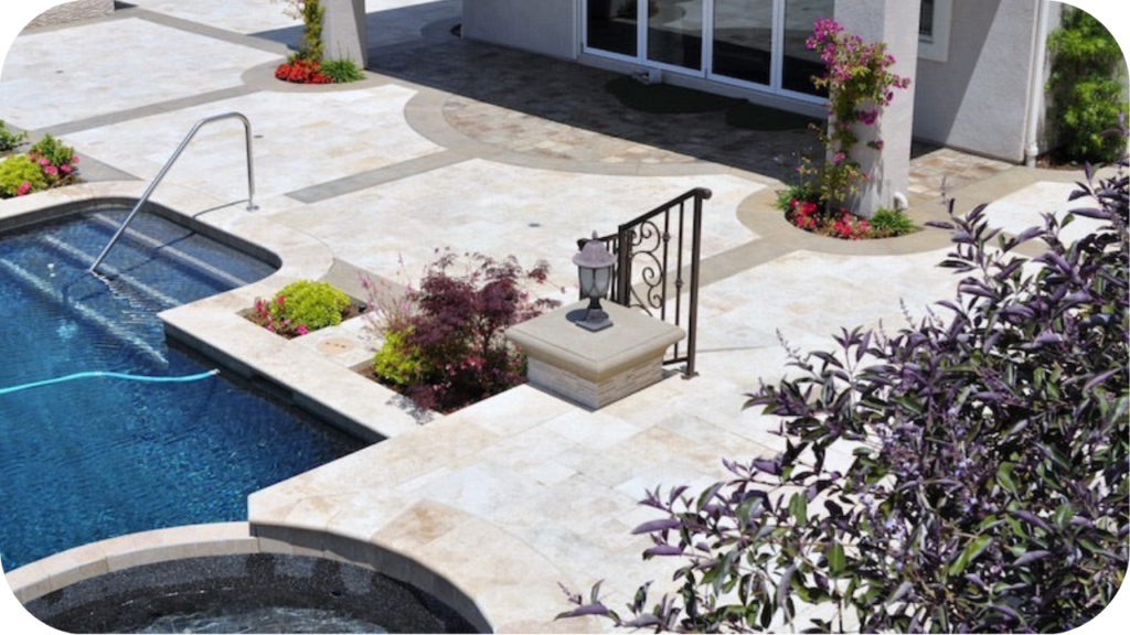 Poolside area with beige travertine tiles, built-in garden planters, and decorative railing adding elegance to outdoor landscaping design.