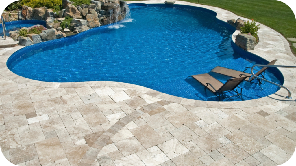 Curved swimming pool with waterfall feature, travertine tile deck, and lounge chairs partly submerged for a stylish outdoor retreat.
