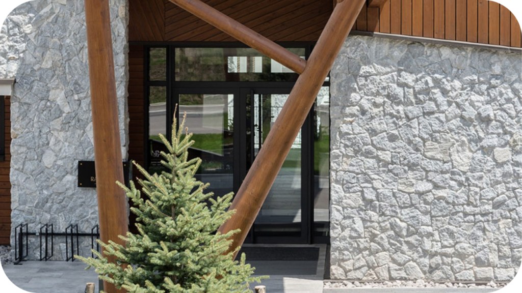 Resort-style hotel entry with icy grey split stone cladding, timber beams and alpine-inspired architectural framing.