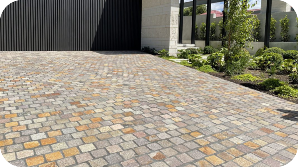 Expansive driveway paved with multi-coloured porphyry cobblestones, combining grey, gold, and earthy tones to create a durable and elegant entrance for a modern home.