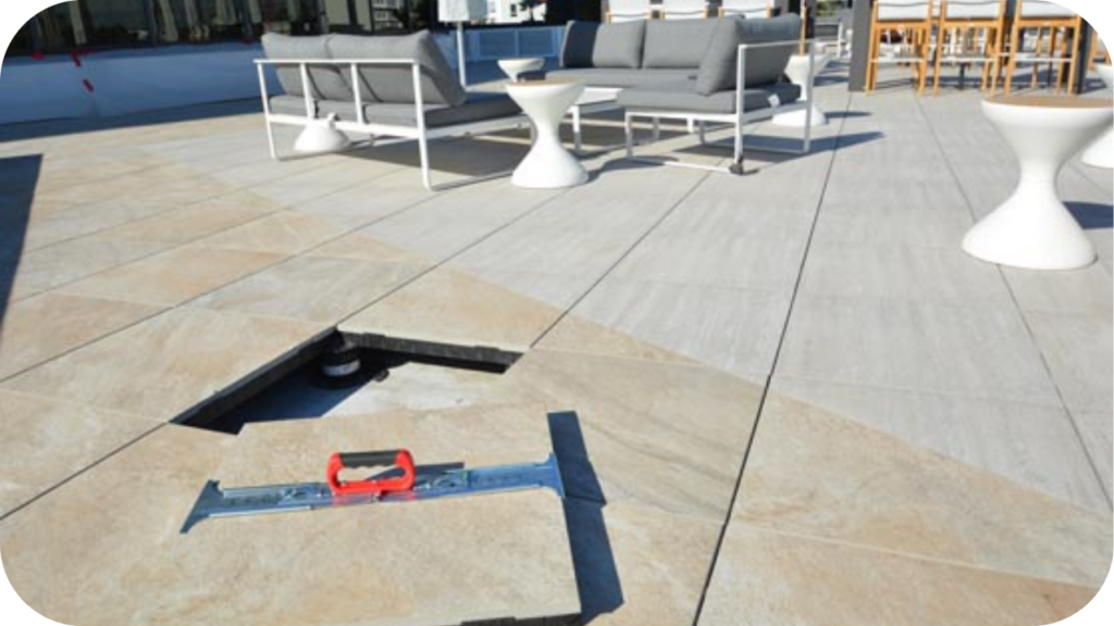 Quartzite pavers on a spacious outdoor terrace with a section lifted for maintenance, a level tool placed on top, and modern seating in the background.