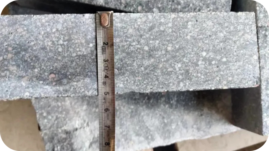 Close-up of grey porphyry cobblestones measured with a ruler, showing thickness and quality for accurate paving installation and durability.