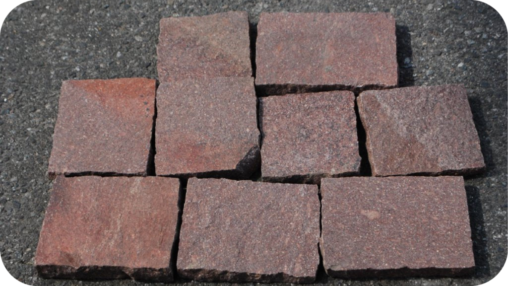 Red porphyry cobblestones neatly arranged on asphalt, highlighting natural colour variations and texture suitable for outdoor paving projects.