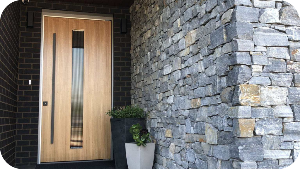 Modern home entrance with stacked grey quartz wall cladding, wooden door, and potted plants creating a contemporary style.