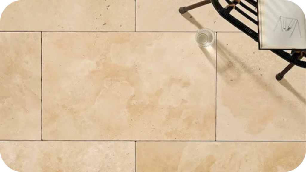 Beige travertine stone pavers with a smooth finish, styled with a chair and glass, showing timeless elegance for modern outdoor spaces.