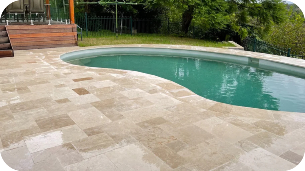 Travertine tiles surrounding a curved swimming pool, showing the elegance and functionality of choosing the right travertine supplier in Melbourne.