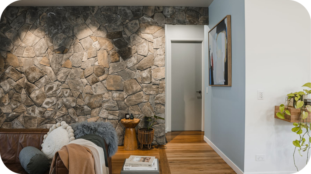 Living room accented with textured stone wall cladding, cosy sofa, soft throws, and timber flooring for natural warmth.