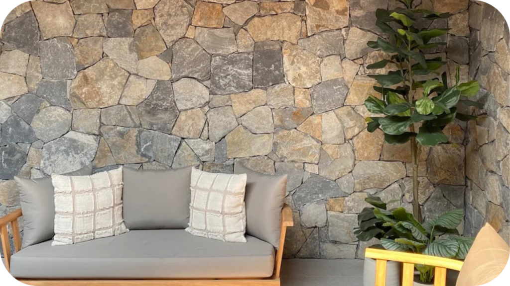 Outdoor seating space with grey stone wall cladding, timber lounge, and lush greenery creating a modern, relaxed vibe.