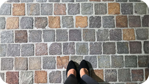 Feet standing on multicoloured cobblestones, showcasing a durable high-traffic paving choice for walkways and plazas.