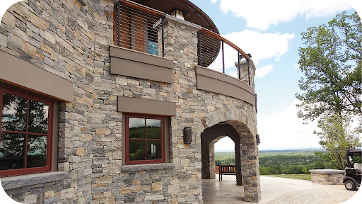 Luxury hotel perched on hillside with castle-style architecture and full-height stone cladding under sweeping views.
