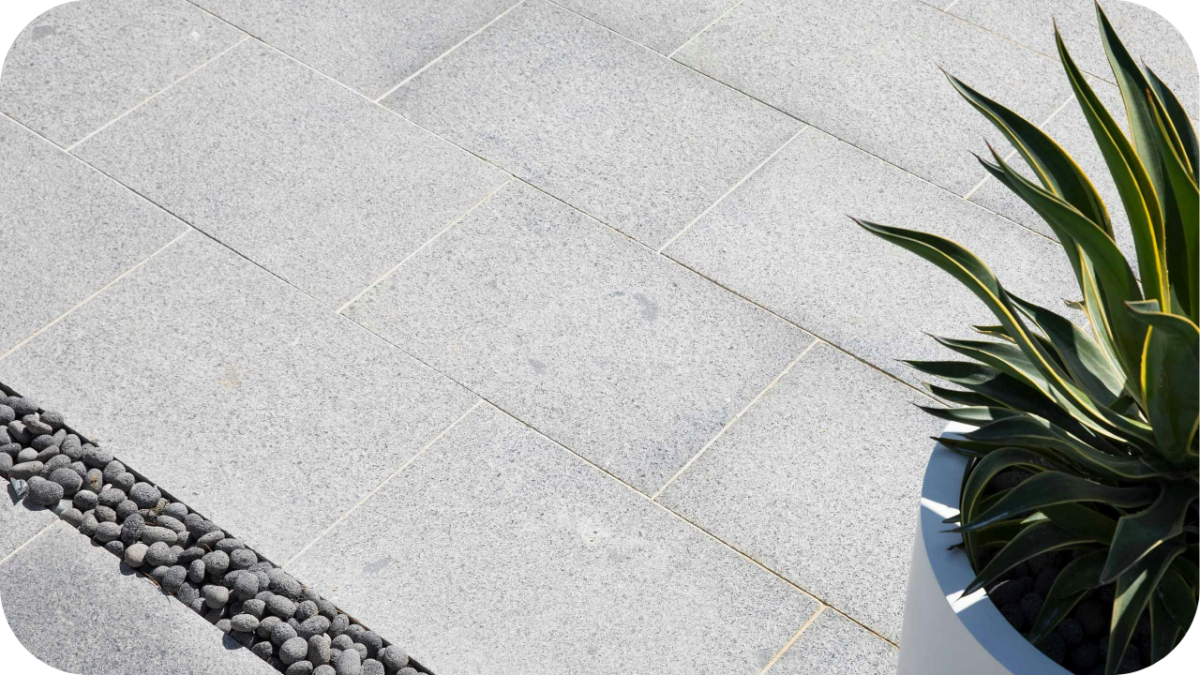 Grey granite pavers with clean lines beside a plant and decorative pebbles, showing durable paving suitable for Australian homes and landscapes.