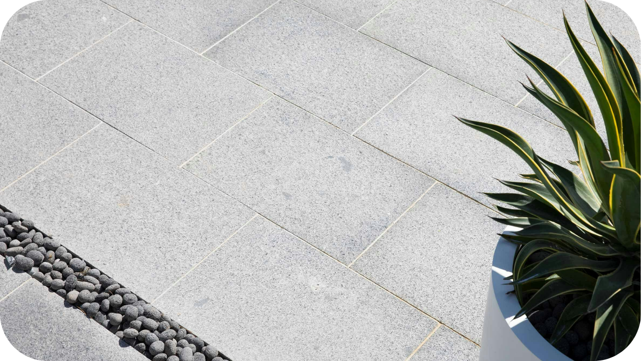 Grey granite pavers with clean lines beside a plant and decorative pebbles, showing durable paving suitable for Australian homes and landscapes.