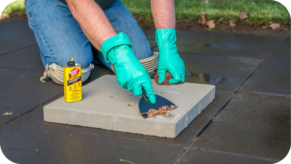  Person in gloves cleaning granite paver with scraper and cleaner, showing simple maintenance steps to preserve durability and natural stone beauty.
