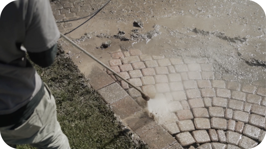  A worker uses a pressure washer to clean a dirty paver walkway that has been laid in a decorative fan pattern.
