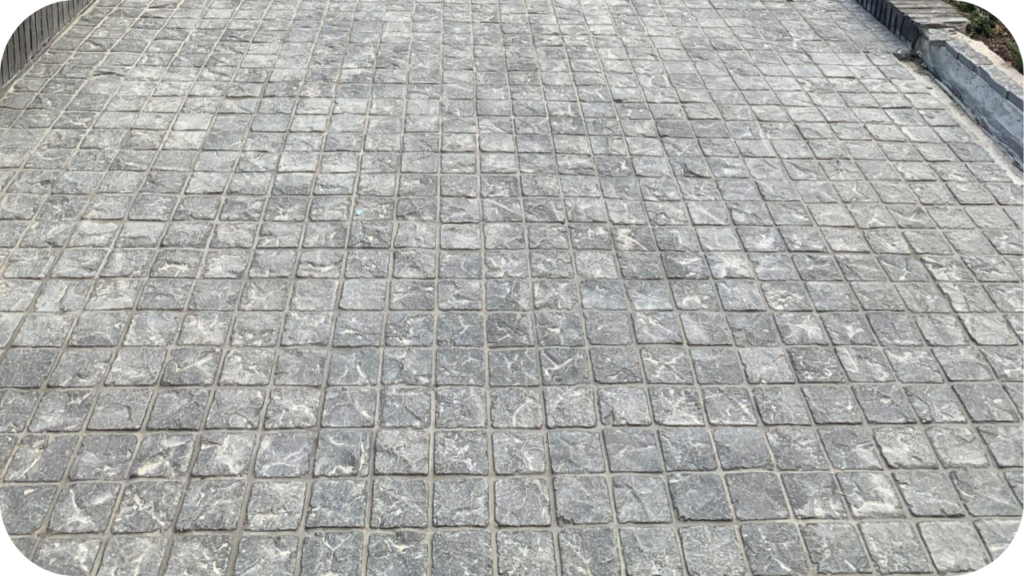 A high-angle view of a paved surface with a neat grid pattern of square, grey cobblestones that have a rough, textured finish.