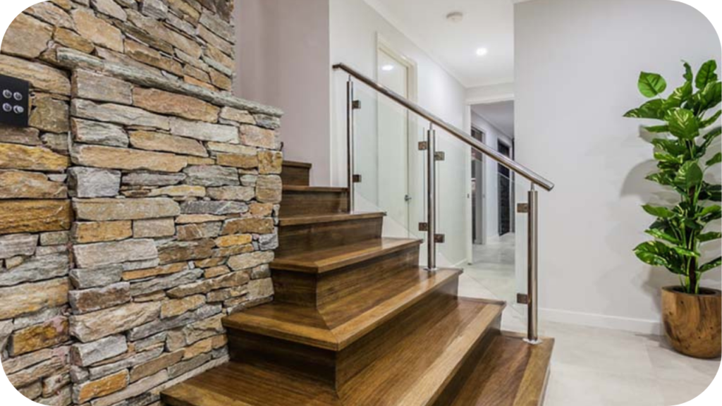 Stacked stone wall feature beside modern timber stairs with glass balustrade, showcasing natural stone texture as the focal design element.