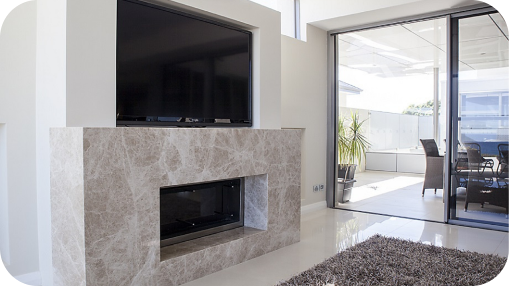 Sleek marble stone fireplace beneath a large flat-screen TV, with sliding doors opening to a sunlit outdoor area.
