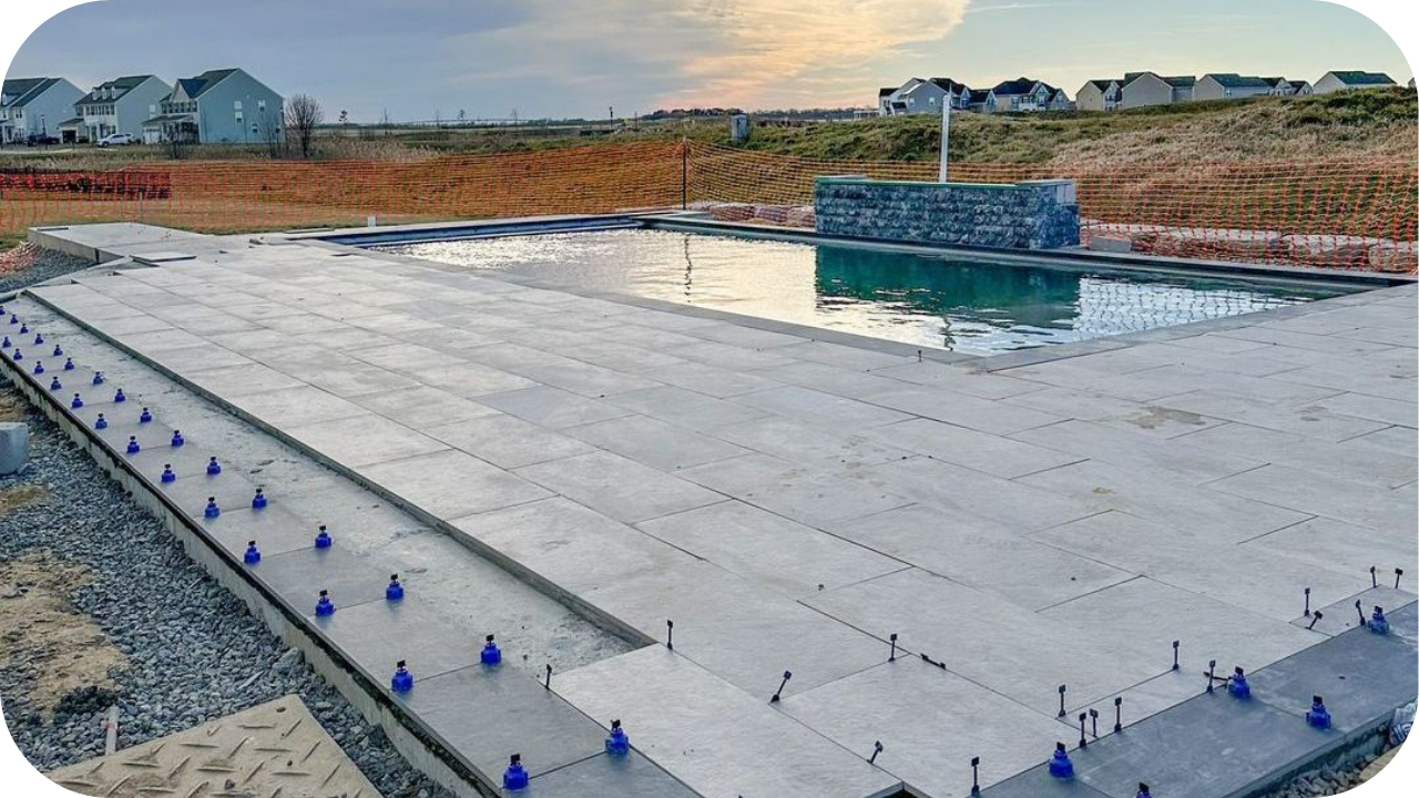 A large swimming pool patio being installed with grey paver stones, using a blue tile leveling system.