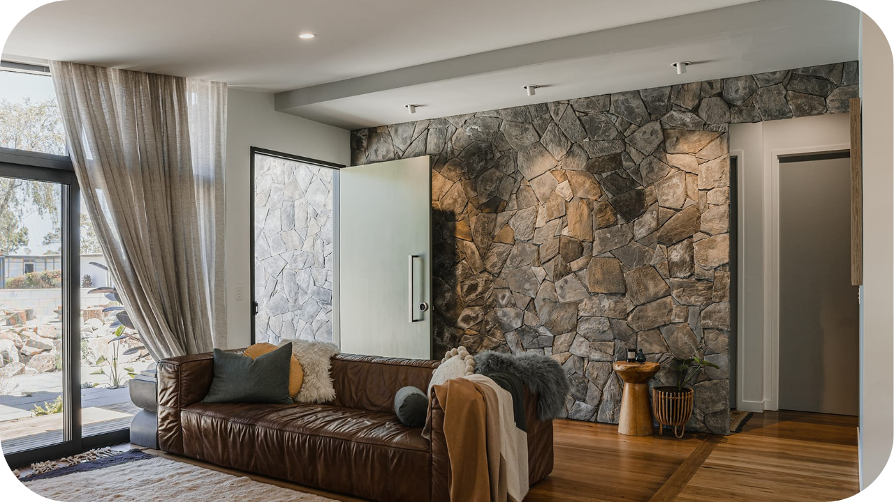 Natural stone feature wall in a contemporary living room with a brown leather sofa, soft lighting, and timber flooring creating a warm, textured interior.