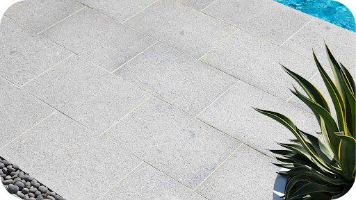 ight grey granite paving beside a pool with a green feature plant, showing how granite handles heat and suits modern Australian outdoor spaces.