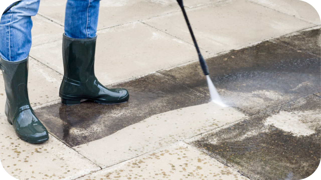 A person in gumboots using a pressure washer to clean outdoor limestone pavers, lifting built-up grime to restore the surface to a fresher, brighter condition.