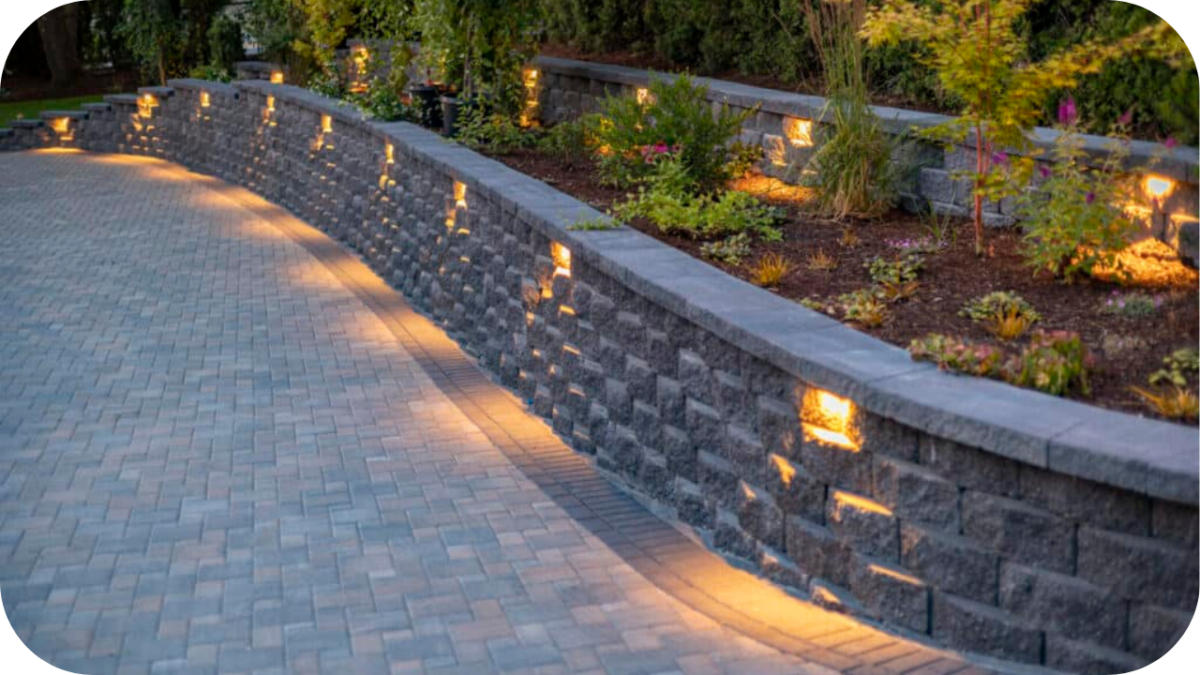 Cobblestone driveway curving beside a tiered retaining wall with warm garden lighting, creating a stable and elegant layout for sloped outdoor areas.