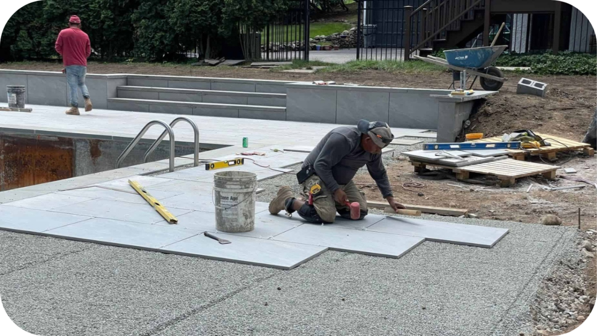 Workers laying large stone pavers around a pool area, levelling and fitting each piece to create a clean and durable DIY paving surface.