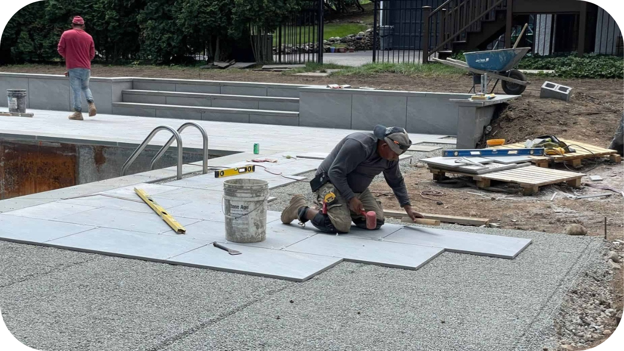 Workers laying large stone pavers around a pool area, levelling and fitting each piece to create a clean and durable DIY paving surface.