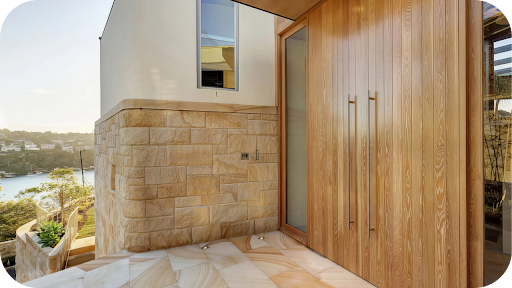 Modern home entrance featuring sandstone cladding and large wooden doors, overlooking a scenic coastal view in Sunshine Coast.