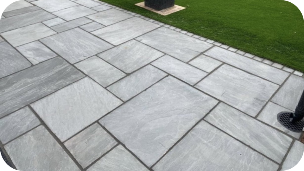 Ashlar pattern natural stone paving in soft grey tones beside a lush green lawn, showcasing a modern layout with varied tile sizes in an Australian outdoor space.