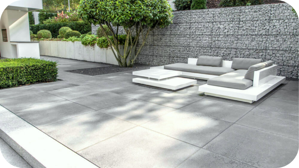 Spacious granite paved patio with modern outdoor furniture, landscaped plants, and a stone retaining wall creating a stylish and durable entertaining area.