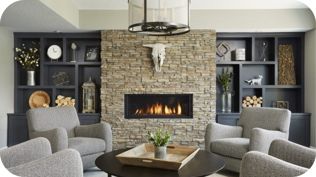 Stacked stone fireplace set within a modern lounge featuring grey armchairs and built-in shelving, creating a warm and stylish gathering space.