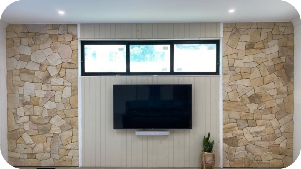 Contemporary living room with a TV mounted on a central panelled feature wall, framed by natural stone cladding on both sides.