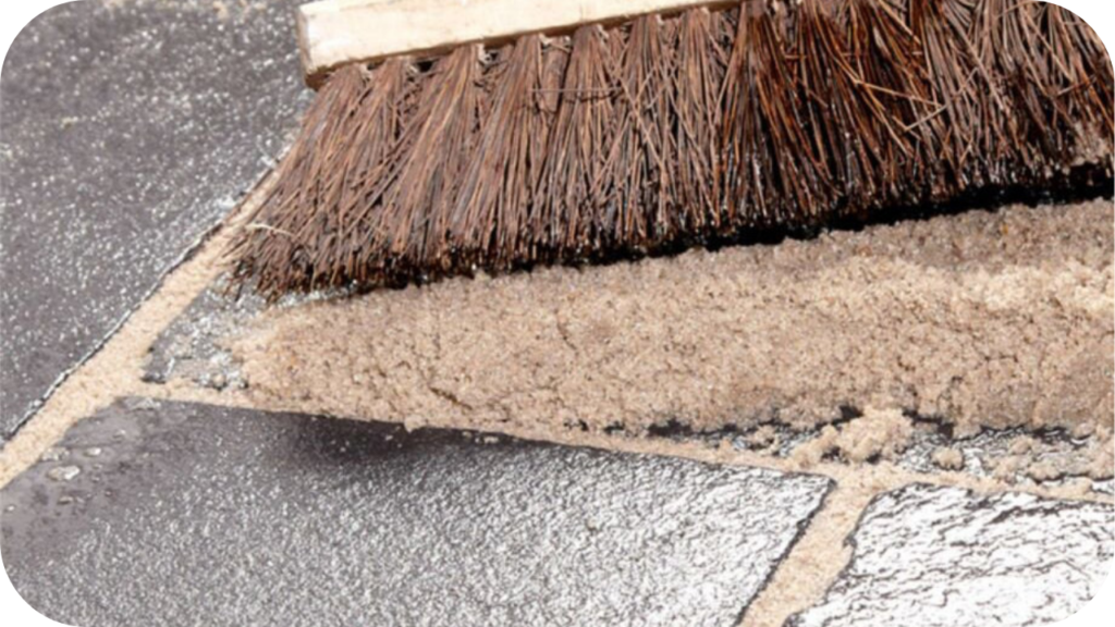 Fresh grout being applied between limestone paver joints with a coarse broom, helping stabilise the bedding layer and maintain a strong, even outdoor surface.