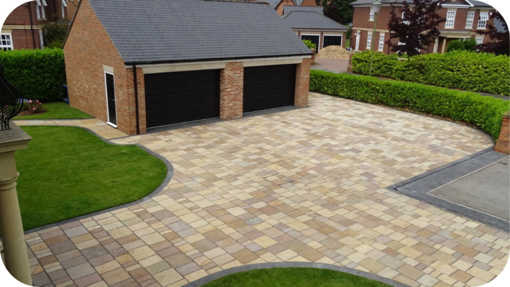 Large driveway featuring light beige and tan paving blocks arranged in a neat pattern, demonstrating clean driveway layout and strong visual design.