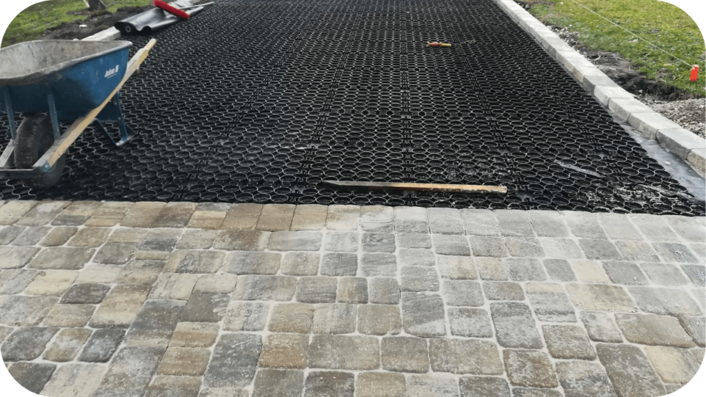 Driveway installation in progress with a permeable grid base and cobblestones, showing proper sub-base preparation for long-lasting driveway stability.
