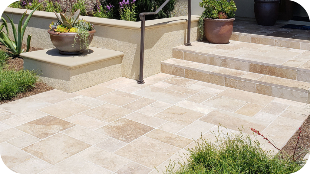 Cream travertine pavers arranged in a French pattern at a home entrance with steps, garden beds and planters creating a bright, welcoming outdoor space.